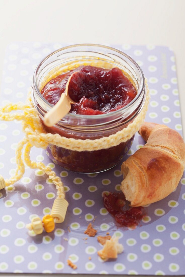 Cranberry jam in jam jar with a piece of croissant