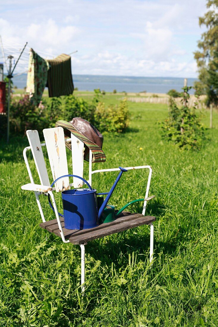 Alter Holzstuhl mit Giesskannen im Garten mit Blick aufs Meer