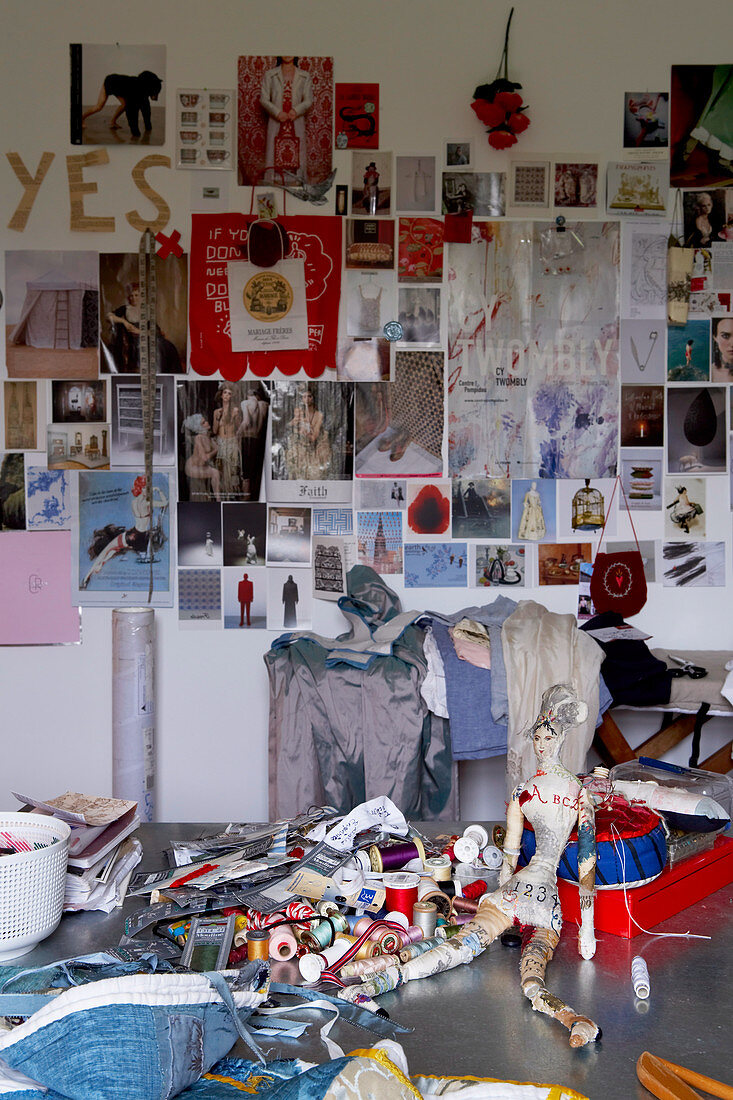 Sewing utensils and fabrics in front of wall covered in postcards