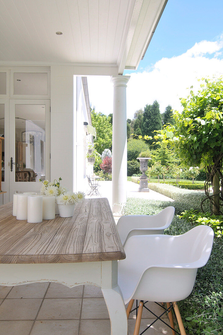 White shell chairs at rustic wooden table on veranda in front of colonial-style house