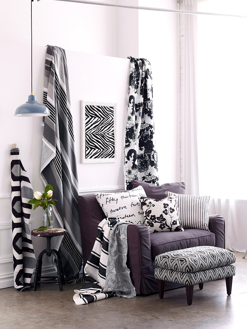 Black and white patterned lengths of fabric next to upholstered armchair with scatter cushions and footstool