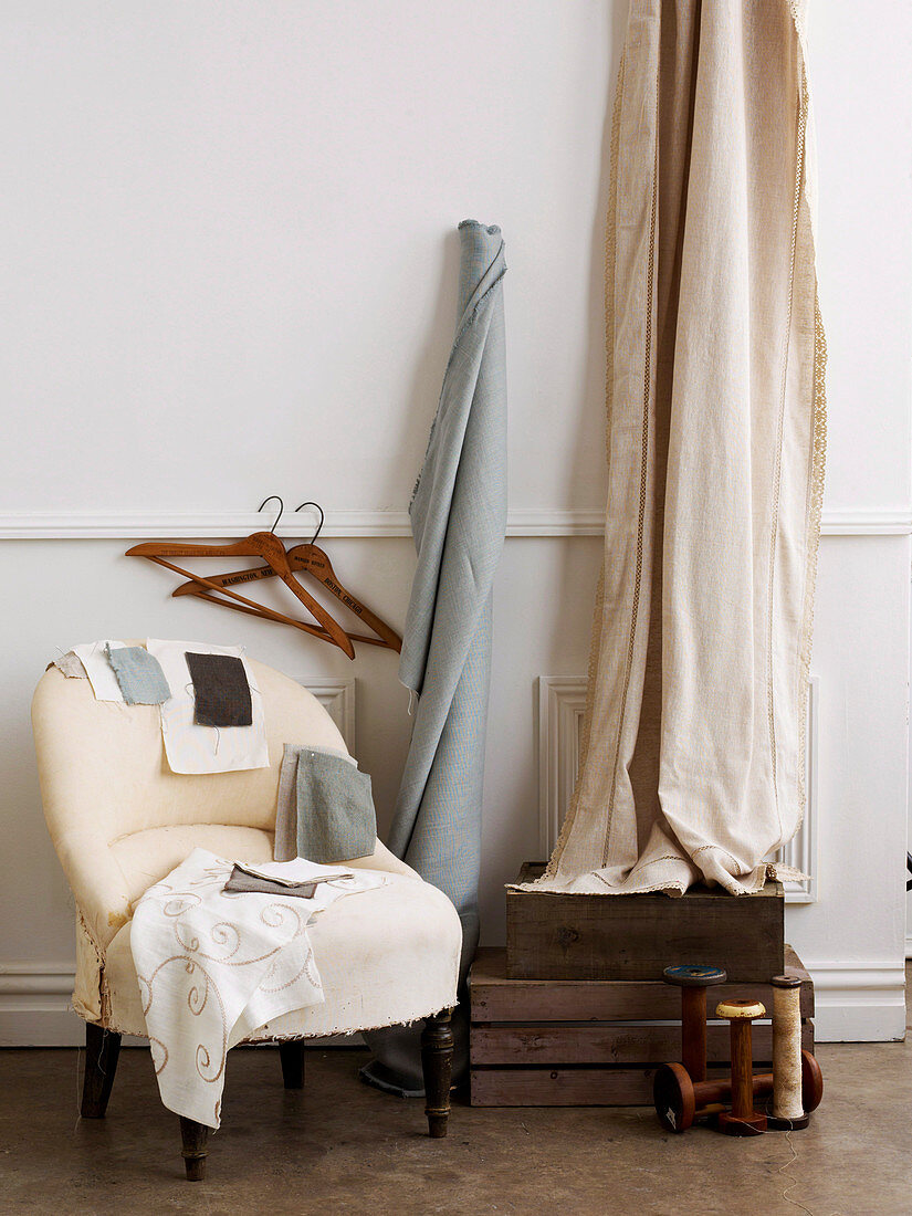 Vintage ladies' armchair next to simple wooden crates and bolts of cloth leant on wall