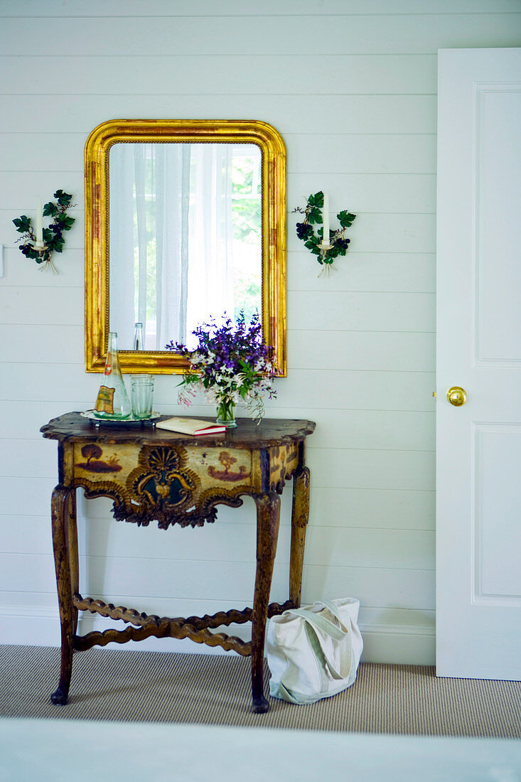 Antiker Wandtisch mit Schnitzereien vor Spiegel mit Goldrahmen in ländlichem Vorraum