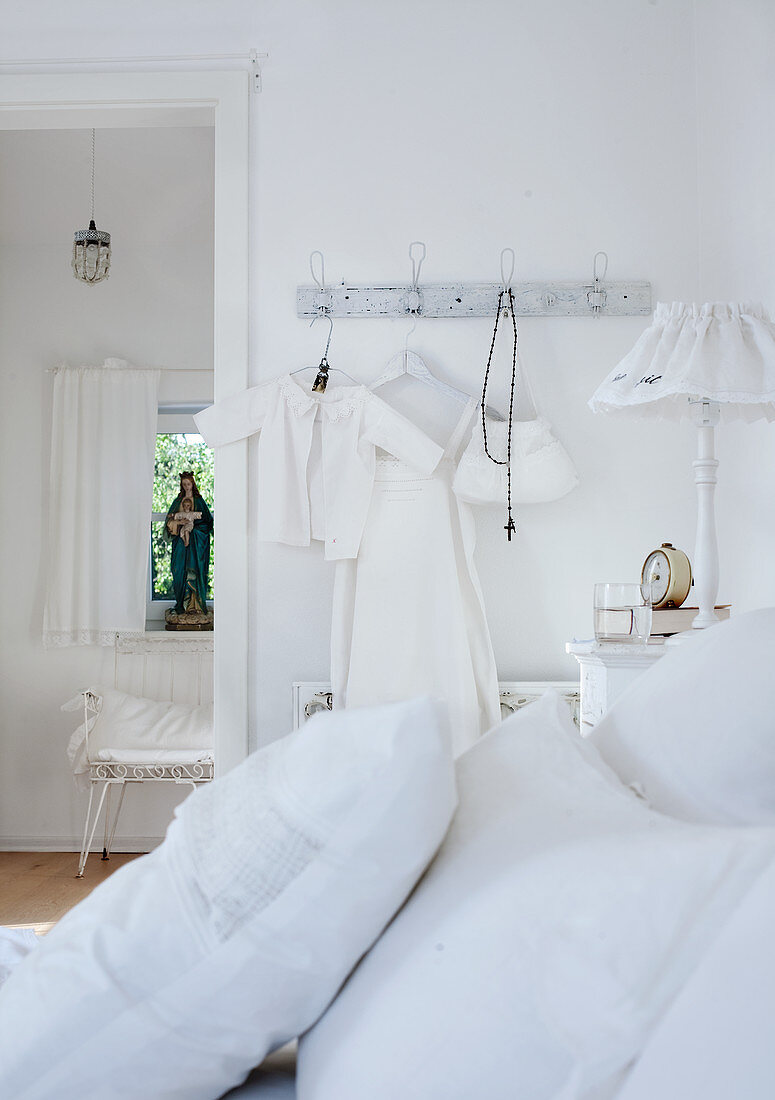 Weissbezogene Kissen auf Bett und aufgehängte Kinderkleider an Wandhaken