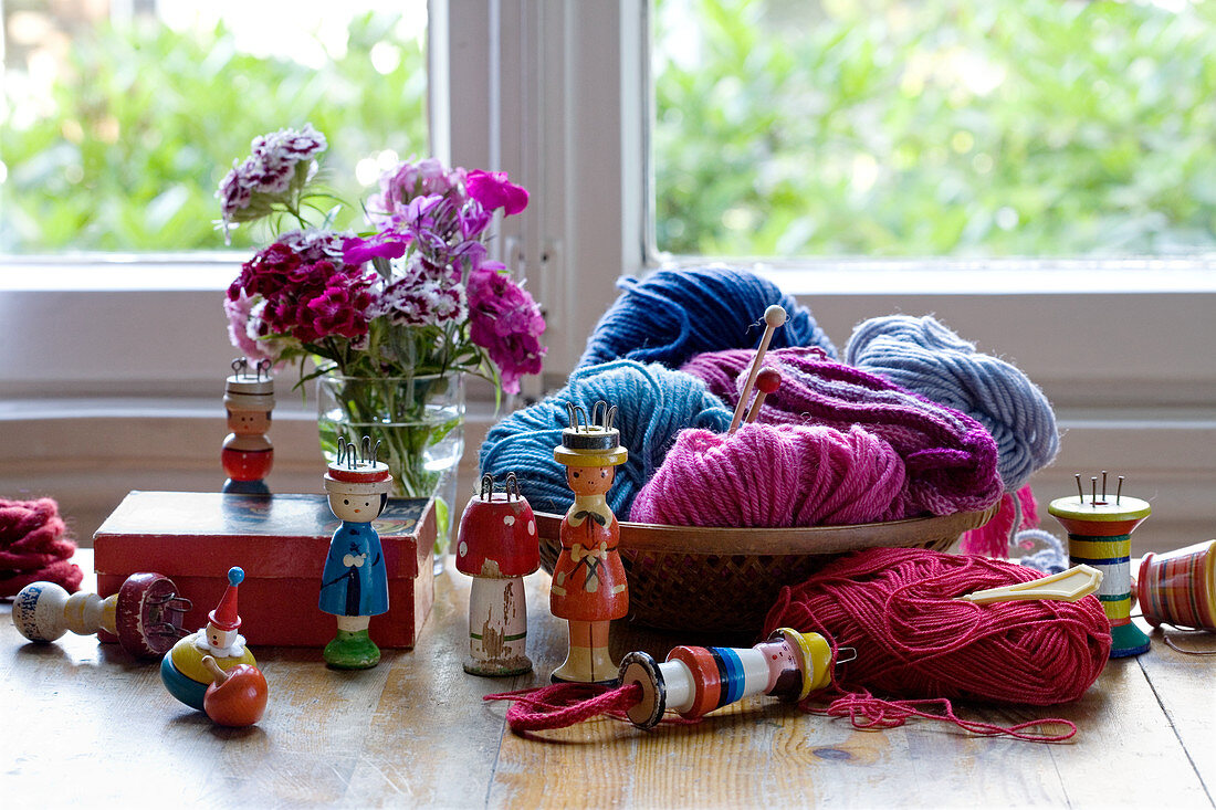 Collection of knitting dollies, wool basket and vase of sweet William in front of window