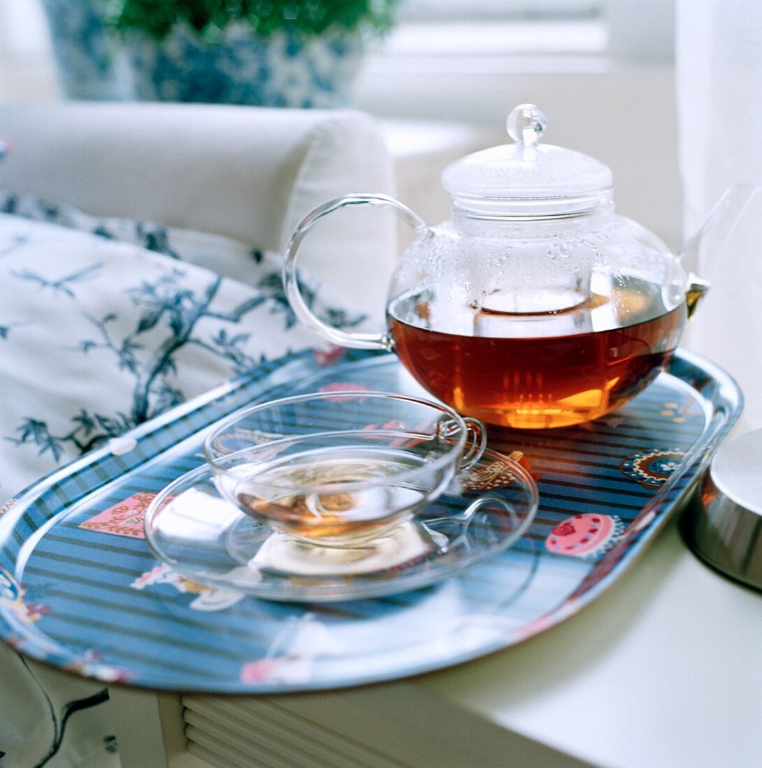 Freshly brewed tea in a glass pot on a tray with a glass cup