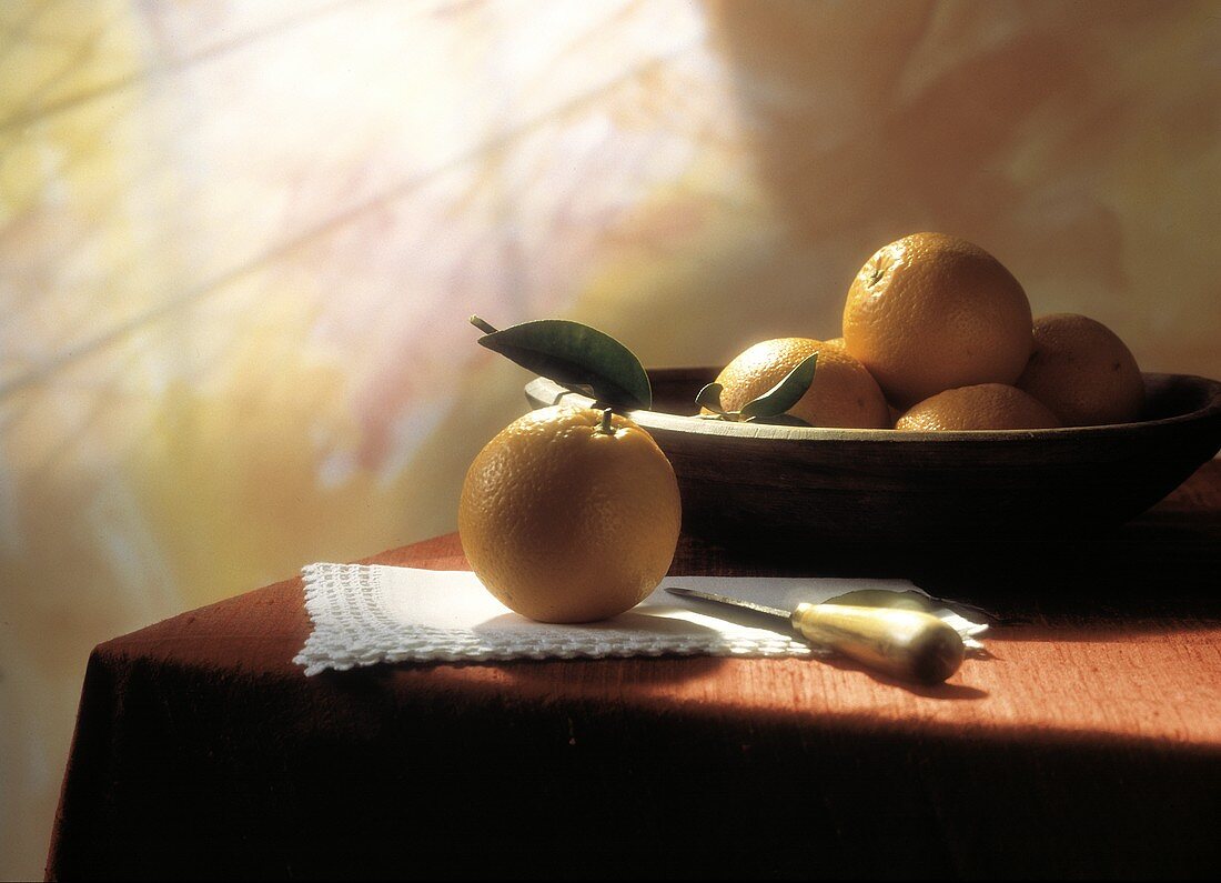 Stillleben: Orange & eine Holzschale mit Orangen auf Tisch