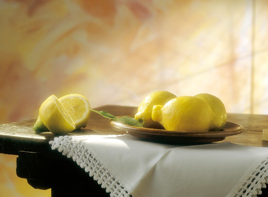 Stillleben: drei Zitronen & eine halbierte Zitrone auf Tisch