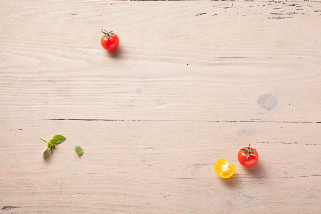 Yellow and red tomatoes and basil leaves on a wooden surface