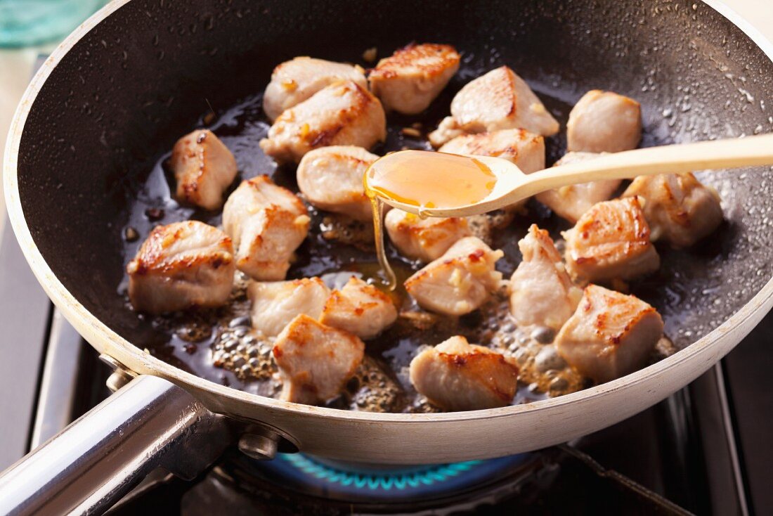 Chicken being fried and drizzled with honey