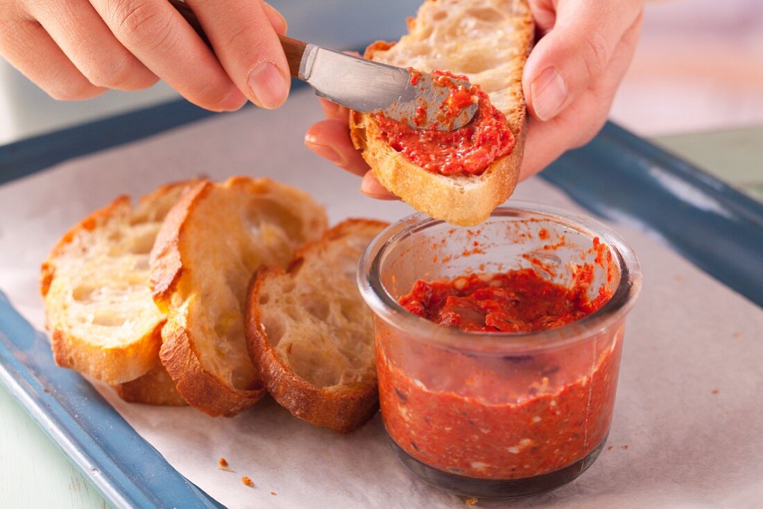 Toasted bread being spread with pepper and olive paste