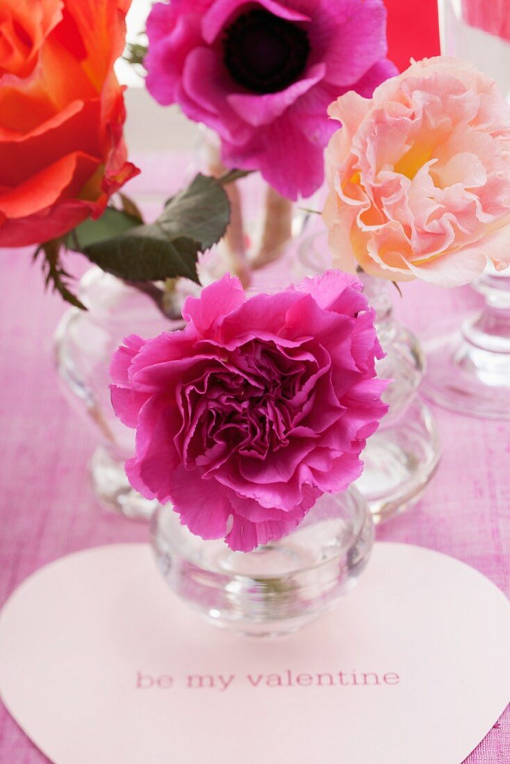 Blumen in Glasvasen und herförmiges Kärtchen mit 'be my valentine' Aufschrift