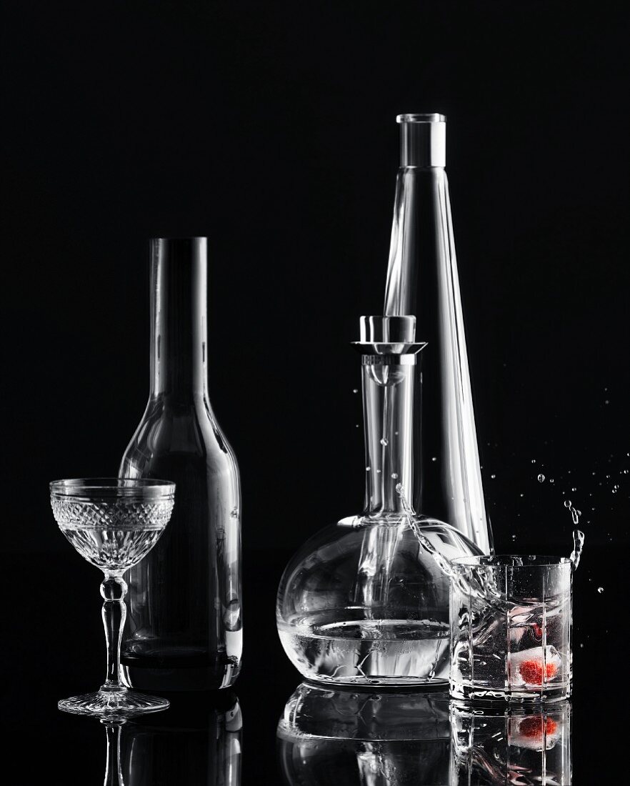 Eiswürfel fällt in Wodkaglas, Weinflasche und Kristallglas