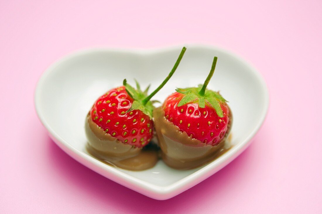 Two chocolate-dipped strawberries in a heart-shaped dish