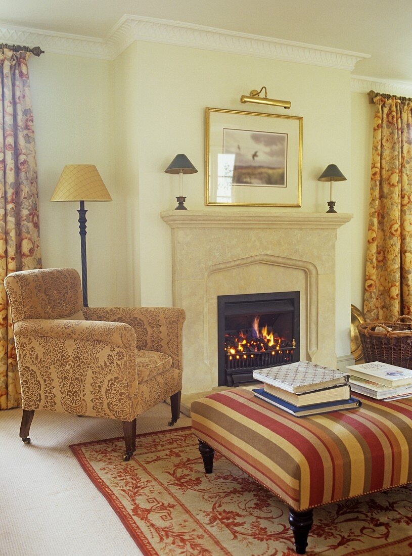 Stack of books on ottoman and reading chair by open fire