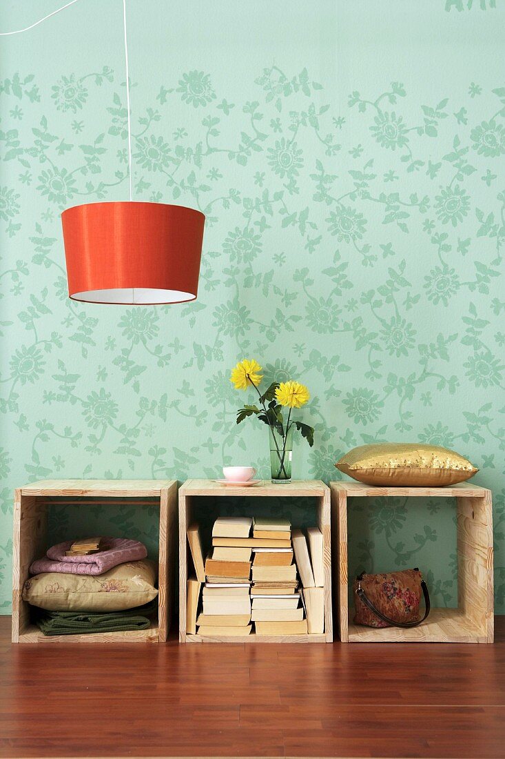 Wooden boxes with stacked books and orange hanging lamp in front of floral wall paper