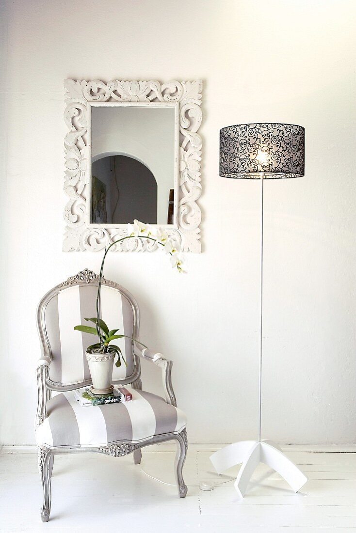 Vintage look, upholstered armchair next to a designer lamp in front of a wall with a mirror