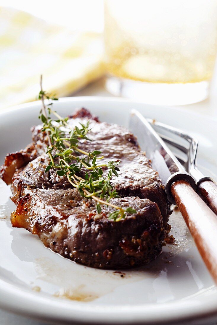 Steak with a Sprig of Oregano on a Plate with Fork and Knife