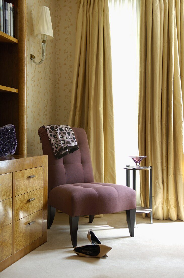 Dainty chair with violet upholstery and high-heeled shoes in corner