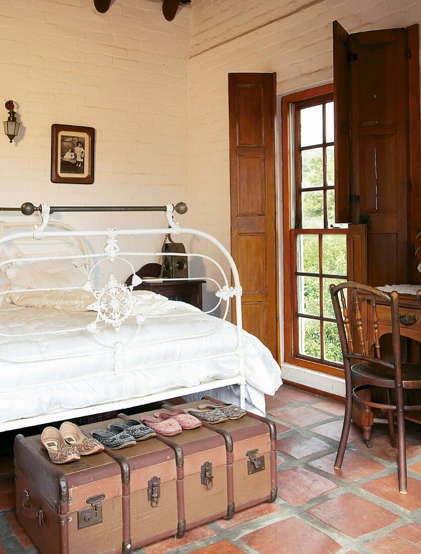 Collection of oriental shoes on old suitcases in front of a wrought iron bed