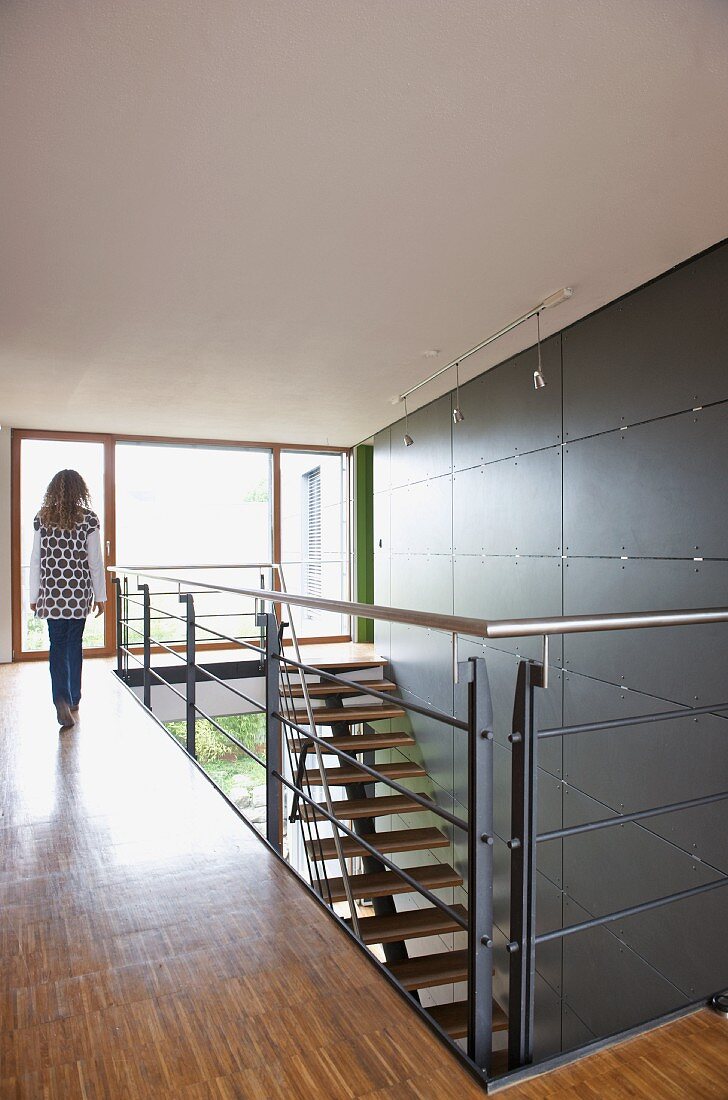 Teenager walking along gallery and staircase against wall with large grey tile panels