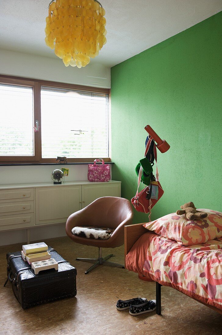 Jugendzimmerecke mit grün getönter Wand und Drehsessel mit braunem Lederbezug neben Bett und Vintage Koffer