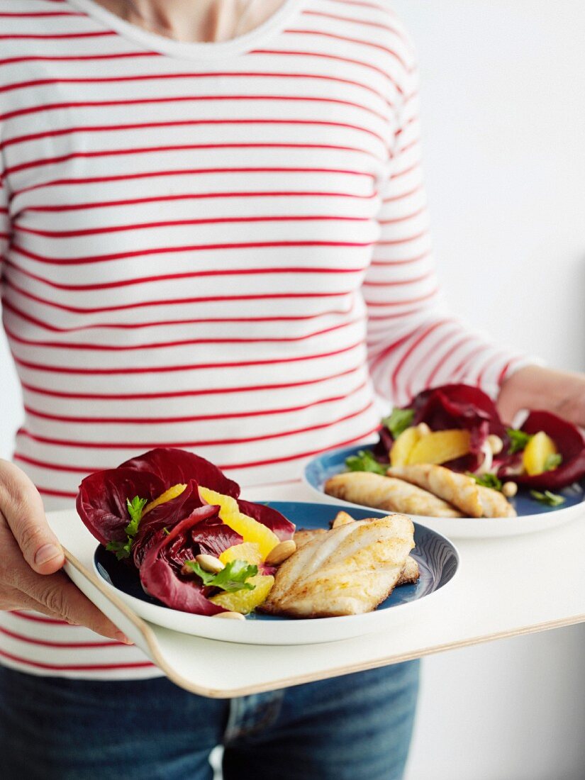 Woman serving fried fish fillets with radicchio and orange salad