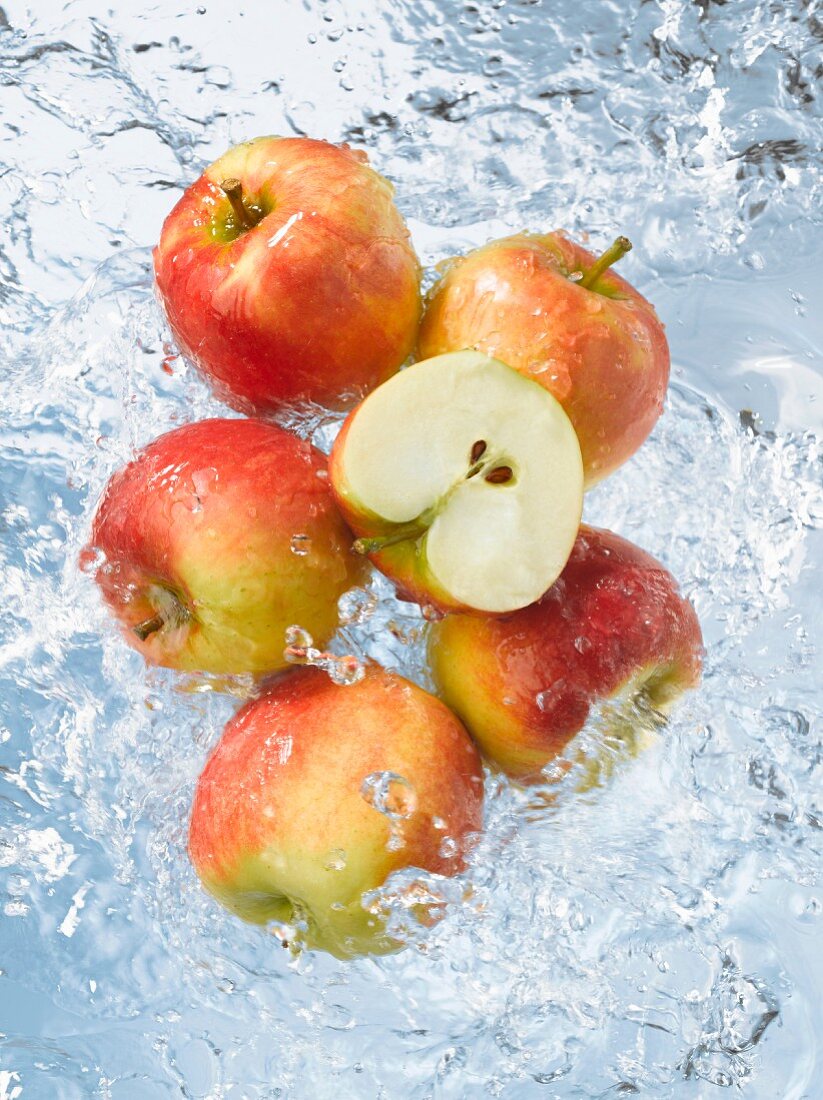 Rote Äpfel, ganz & halbiert fallen ins Wasser