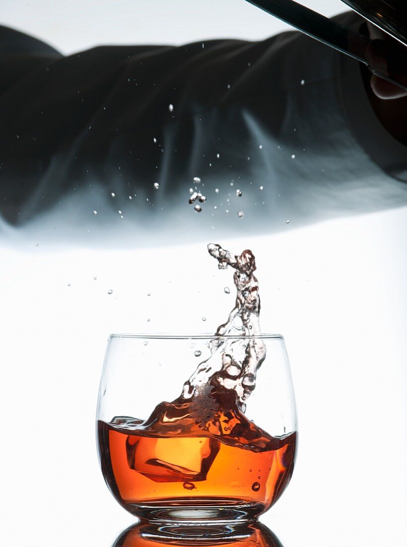 Kellner läßt Eiswürfel von Eiszange in Cocktailglas fallen