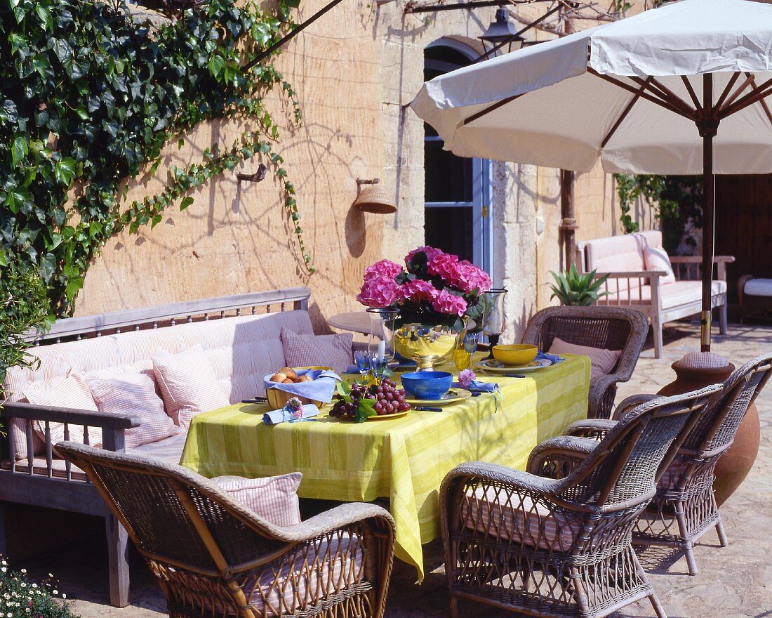 Sommerlich gedeckter Tisch mit Rattansesseln im Freien