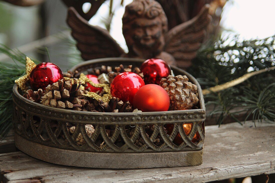 Heart-shaped basket filled with pine cones and baubles in front of iron angel figure