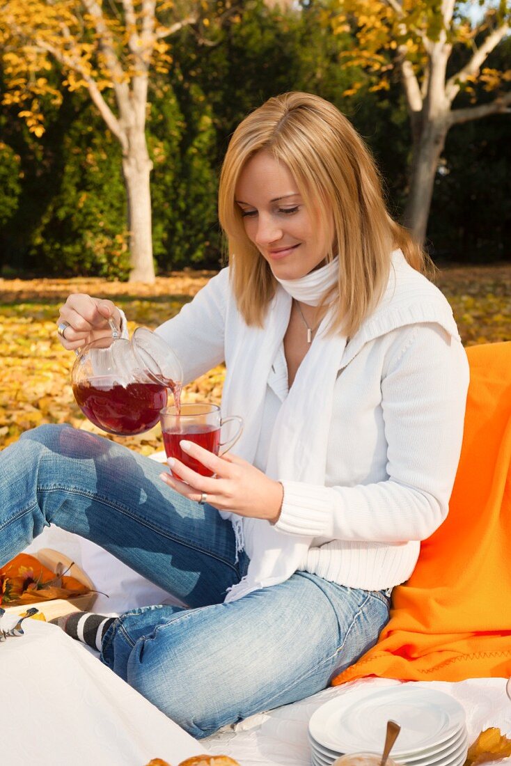 Frau trinkt Tee beim herbstlichen Picknick