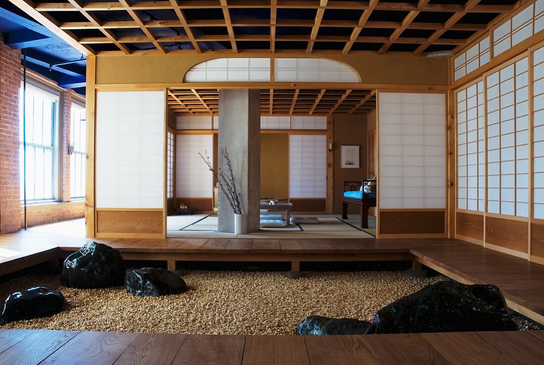 Foyer with platform and gravel floor in front of open, Japanese sliding walls leading to meditation room in industrial hall