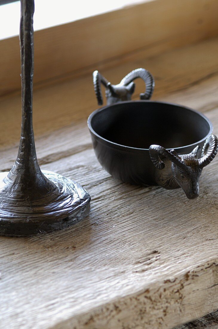 Small metal bowl decorated with ibex heads next to base of table lamp on vintage wood surface