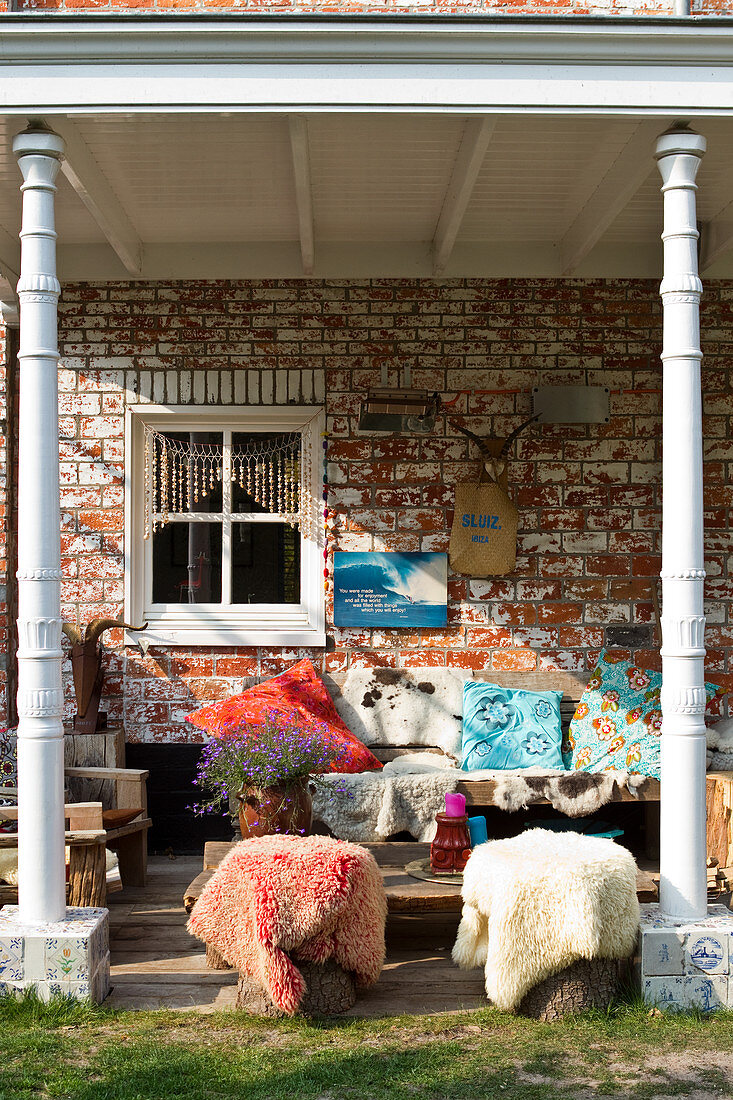 Seats with colourful cushions and animal furs on a covered terrace in front of a historic brick facade