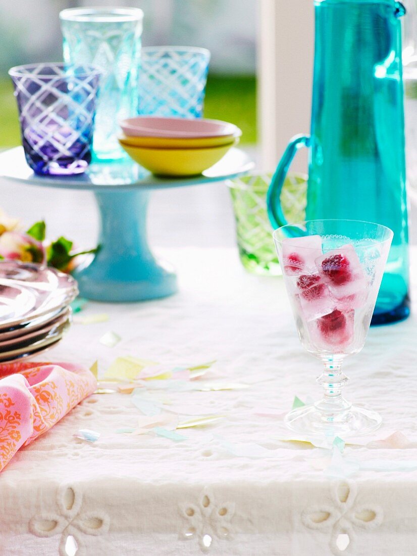 Glass with raspberry ice cubes on a table set for summer