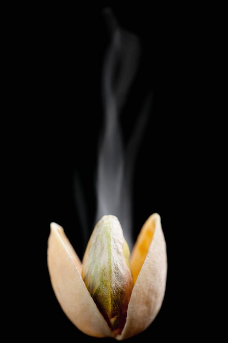 A steaming, opened, toasted pistachio against a black background