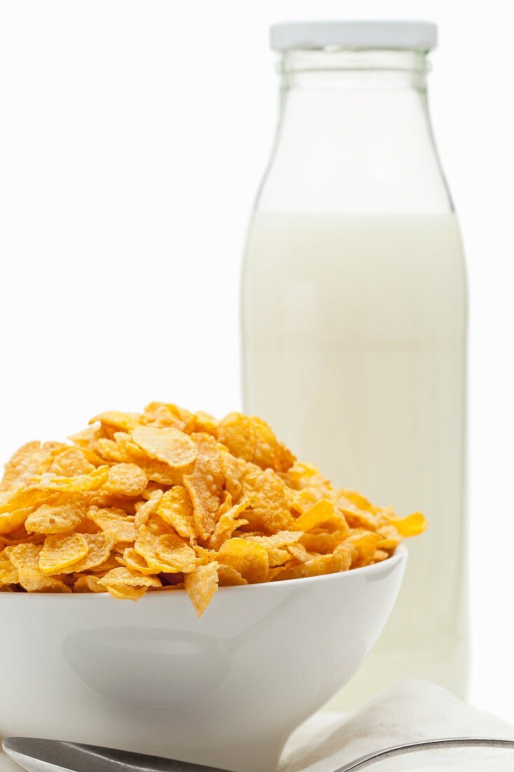 Cornflakes in weisser Schüssel und eine Flasche Milch