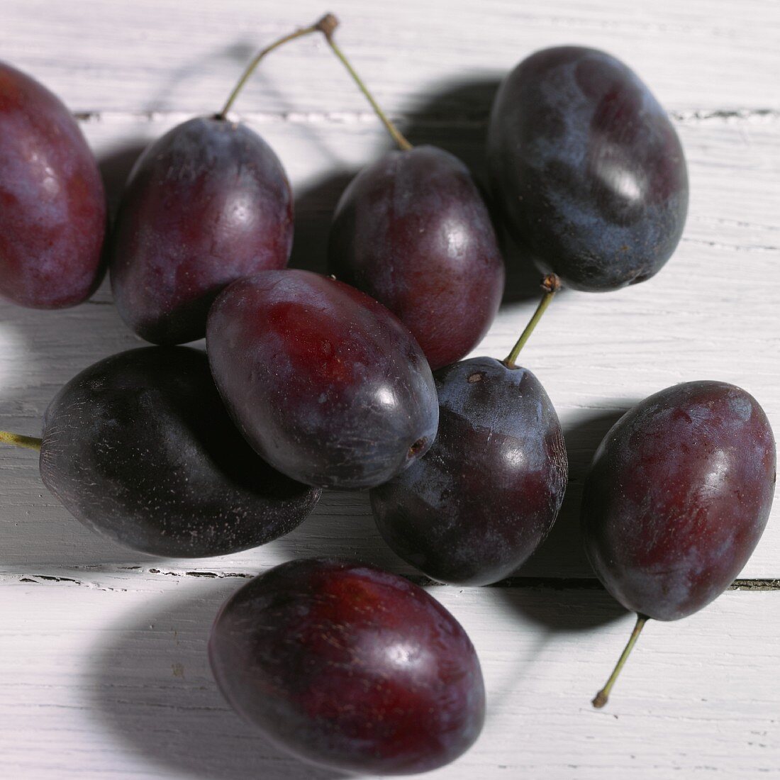 Several plums on a white wood surface