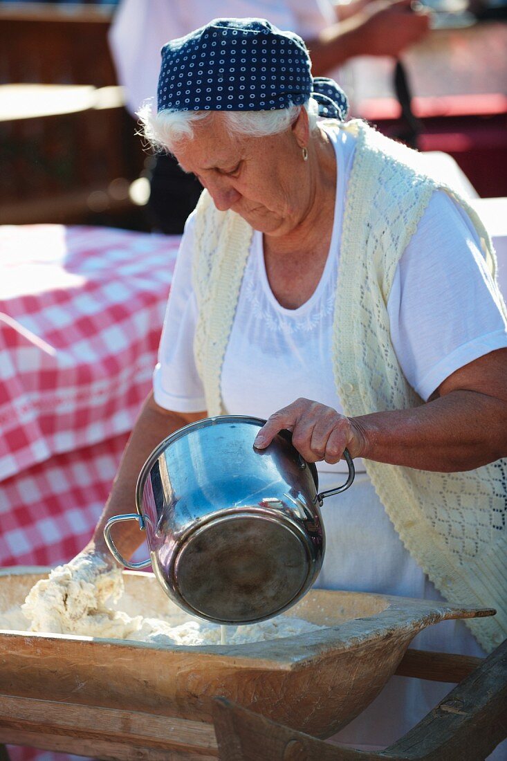 An elderly woman making bread dough in a kneading trough (Hungary)