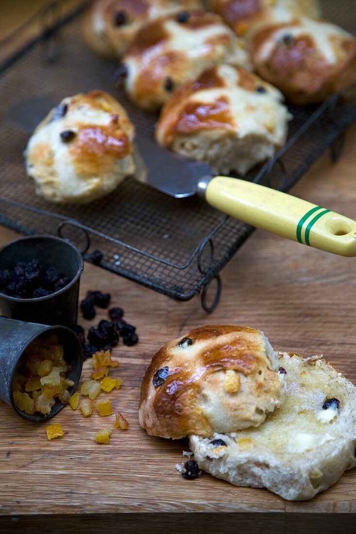 Freshly Baked Hot Cross Buns on a Cooling Rack; One Halved with Butter