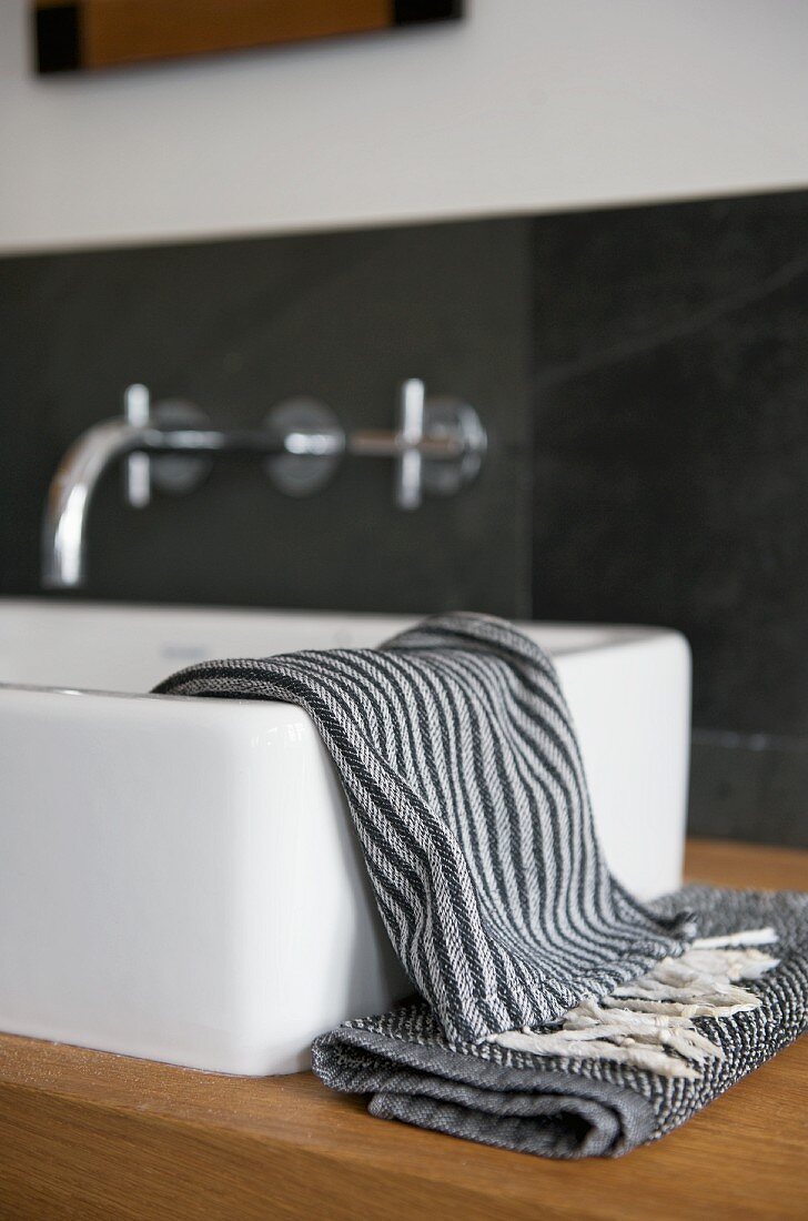 Small towels in shades of grey on wooden washstand with modern countertop washbasin