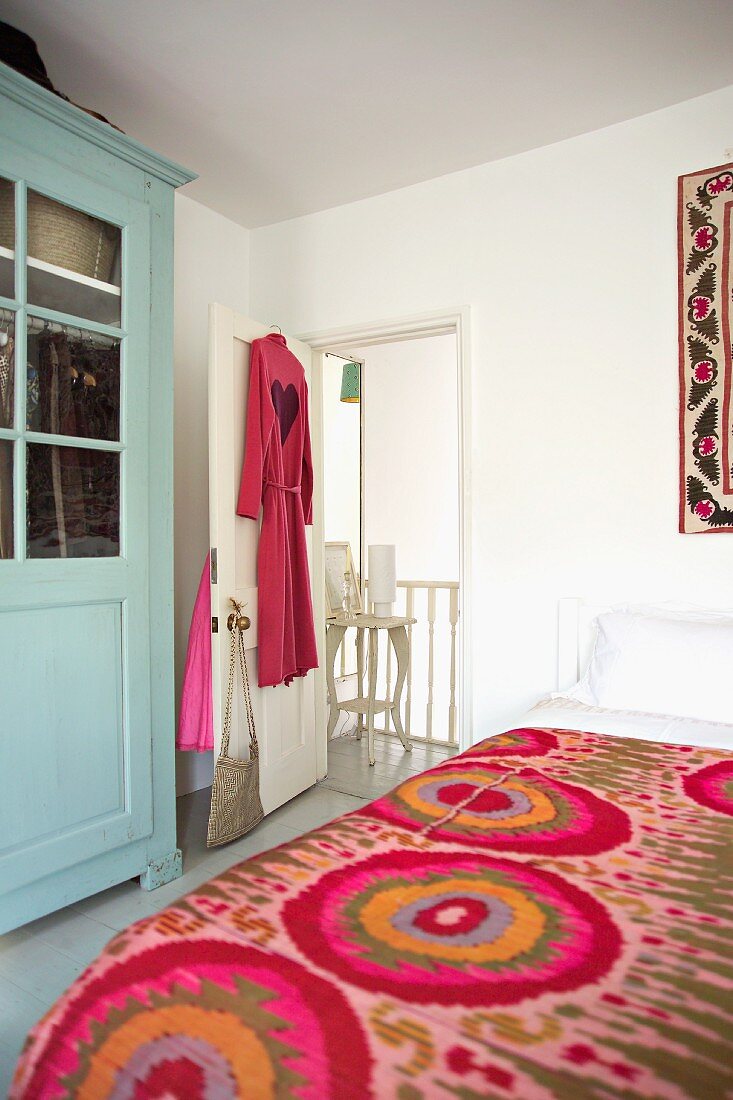 Feminines Schlafzimmer mit poppiger bunter Tagesdecke, rotem Herzchen-Bademantel und pastellblauem Landhausschrank