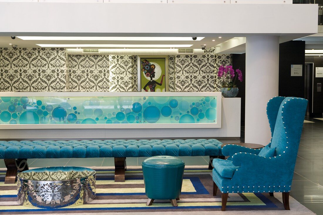 Lounge area in foyer with upholstered couch, blue wingback armchair and long counter