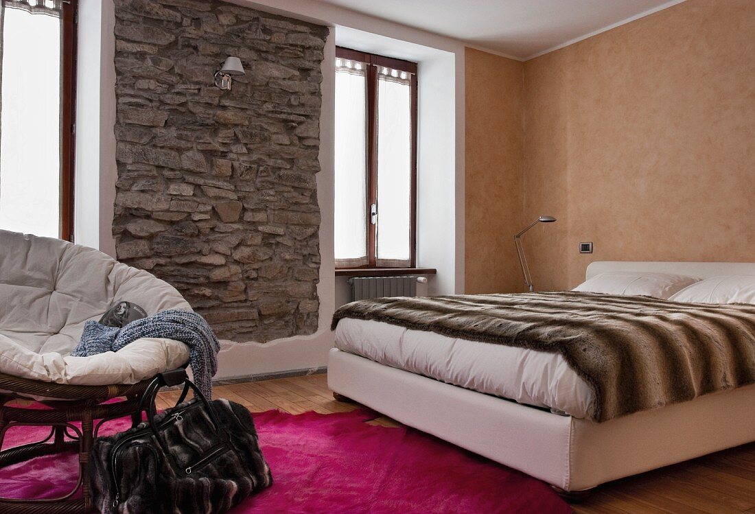 Bedroom in warm earthy shades with framed, rustic stone wall and animal-skin-patterned throw on bed
