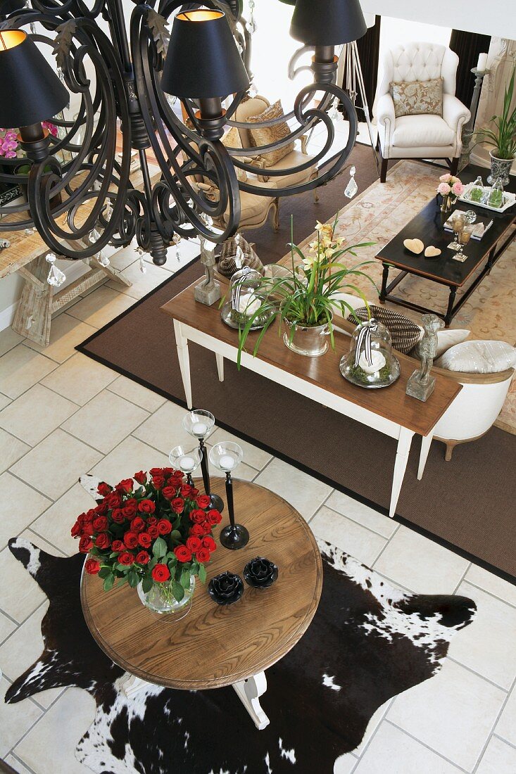 Offener Wohnraum mit Tierfell und schwarzem Kronleuchter; darunter ein großer Strauss roter Rosen auf einem runden Tisch