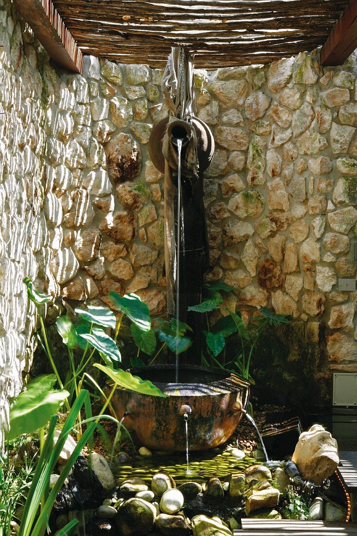 Brunnen vor halbrunder Natursteinmauer mit Weidendach