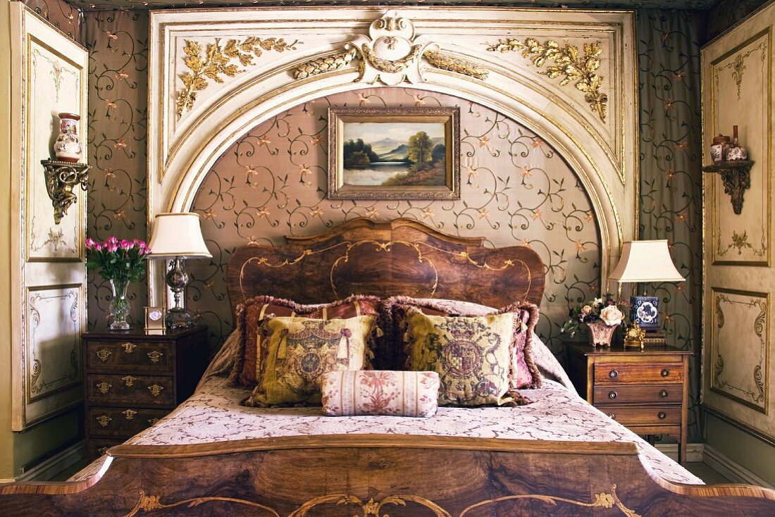 Pile of cushions on bed with antique wooden frame in front of Rococo wall panel in the shape of a portal