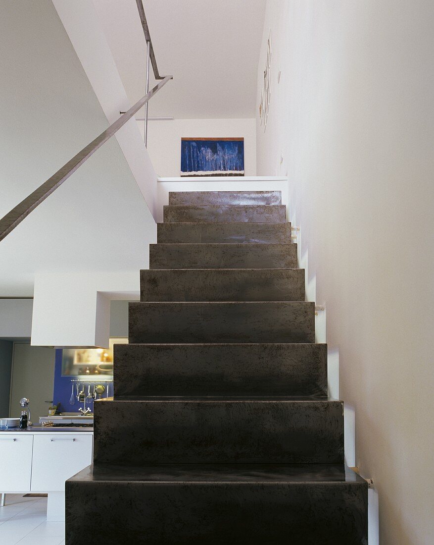 Simple, dark, steel plate staircase with handrail in open-plan interior