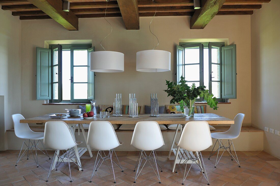 Dining area with white shell chairs and designer pendant lamps in renovated country house